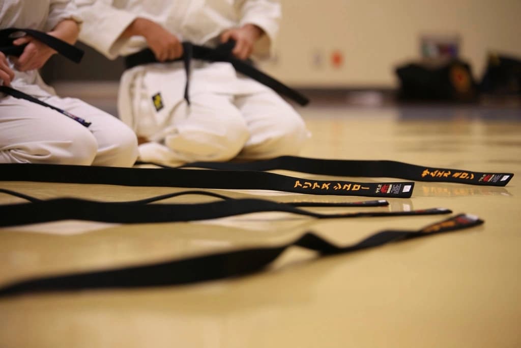 Martial arts students kneeling on a dojo floor with black belts laid out in front of them