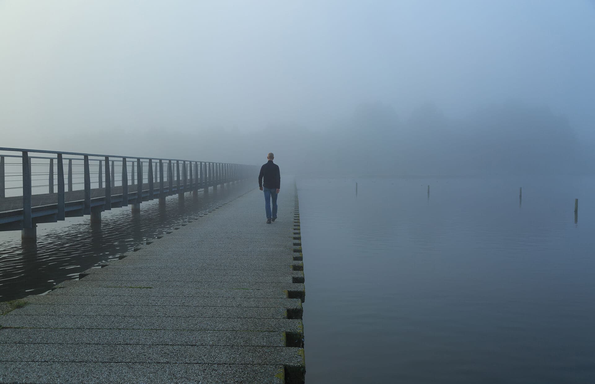 A pier stretching into morning fog over still water