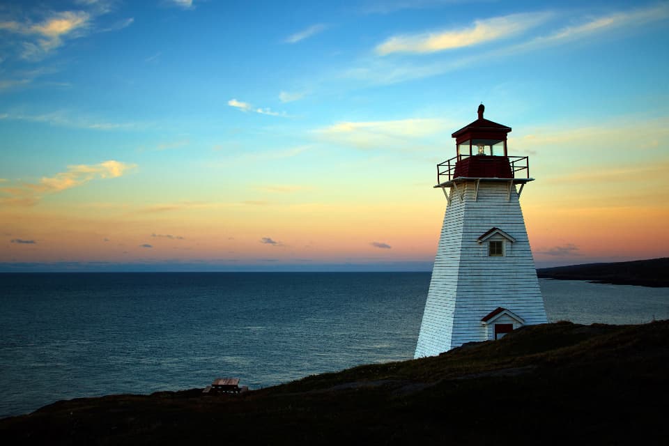 A white lighthouse glowing at sunset above calm water